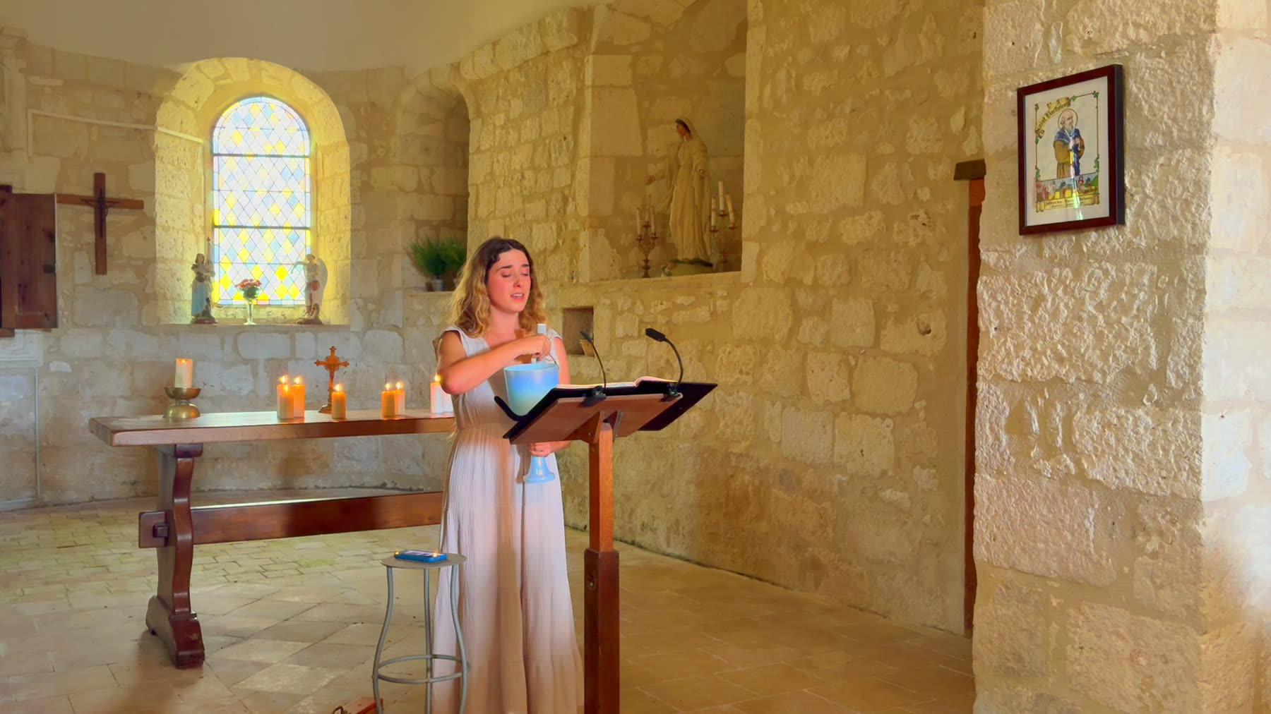 Julie singing at a wooden lectern in a limestone church, sunlight through a small arched window, candles on the altar behind her.